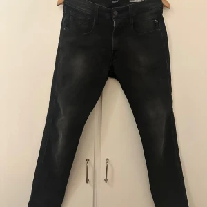 Svarta jeans från Replay - Säljer ett par snygga svarta Replay Anbass jeans i slim fit. De är i mycket bra skick och har en klassisk femficksdesign med dragkedja och knapp. Perfekta för både vardag och fest! 🖤 storlek 31