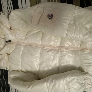 Vit dunjacka från Moncler - Säljer en snygg vit dunjacka från Moncler i nyskick. Jackan har en quiltad design med dragkedja och en praktisk huva. Perfekt för kalla vinterdagar. Den har en cool ficka med Moncler-logga på ärmen. Supervarm och stilren nfc funkar kommer med tags. 