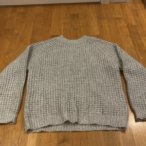 Grå stickad tröja från 157 - Säljer en supermysig grå stickad tröja från 157. Perfekt för kyliga dagar med sin tjocka och varma textur. Tröjan har långa ärmar och en klassisk rund halsringning. Passar perfekt till både jeans och kjol för en avslappnad look.