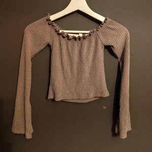 Brun ribbad topp från NLY Trend - Säljer en snygg brun ribbad topp från NLY Trend. Den har långa ärmar och en söt volangdetalj vid halsringningen. Perfekt för höst och vår, och kan stylas både upp och ner beroende på tillfälle. Toppen är i mycket bra skick och redo för en ny garderob!