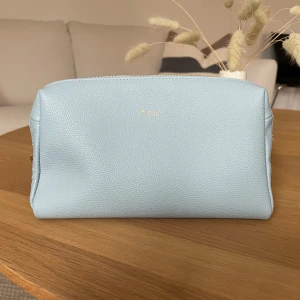 Ljusblå necessär från Moncrief - Säljer en superfin ljusblå necessär Den är i skinn och har en praktisk dragkedja i guld. Perfekt för att hålla ordning på dina småsaker. Stilren och enkel design som passar alla tillfällen! HELT NY köpt för 1200kr