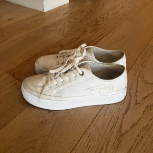 Vita sneakers från Tommy Hilfiger - Snygga vita sneakers från Tommy Hilfiger med snörning och en diskret logga på hälen. Skorna har en stilren design med en tjock sula och texturerad yta som ger en modern look.