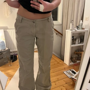 Beige cargopants - Säljer ett par beige cargopants med låg midja och raka ben. Byxorna har flera fickor och en knappstängning framtill. Perfekta för en avslappnad stil.