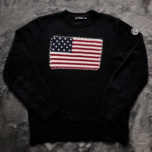 Stickad tröja med USA flagga - Säljer en svart stickad tröja från North Sails med en stor amerikansk flagga på framsidan. Tröjan har långa ärmar och en rund halsringning. Perfekt för en stilren och avslappnad look. Storlek L men passar även M. Har en lagad skada som syns på bilderna, pris går att diskutera✅