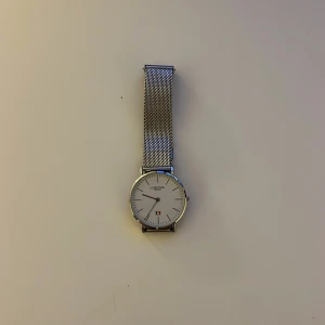 Silverfärgad klocka med mesh-armband - Stilren klocka från Vesaro med en minimalistisk design. Den har en vit urtavla och ett silverfärgat mesh-armband. Klockan har en datumvisare och en elegant boett. Perfekt för en modern och tidlös look. Den har inga batterier men man kan fixa det billigt man får också med ett extra fodral