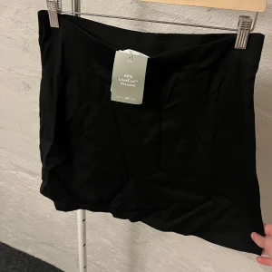 Svart kortkjol - Snygg svart kortkjol i ett mjukt och stretchigt material. Perfekt för en stilren look. Kjolen har en enkel design utan detaljer och är lätt att matcha med olika toppar. Oanvänd, lappen sitter kvar. 