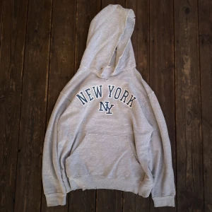 Grå distressed hoodie - Säljer en grå hoodie med texten 'New York' tryckt på framsidan. Mycket distressing, se bild.