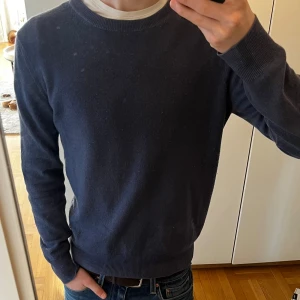 Mörkblå kashmirtröja från BRAUN - Säljer en elegant mörkblå kashmirtröja från BRAUN. Tröjan är långärmad och har ribbade muddar vid ärmslut och nederkant. Perfekt för kyliga dagar och ger en lyxig känsla. Passar både till vardags och mer uppklädda tillfällen. Har tyvärr fått ett pytte hål vid nacken och är något nopprig, se bilder. Hör gärna av vid frågor, funderingar eller prisförslag.