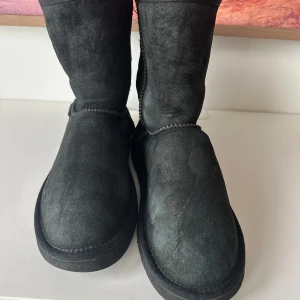 Svarta boots från UGG - Säljer ett par svarta boots från UGG i mocka. De har en klassisk design med mjukt foder inuti för extra värme. Perfekta för kyligare dagar. Välanvända men mycket kvar att ge. Nyimpregnerade och klara att använda🩵🩷 Lappen har lost at lite där bak