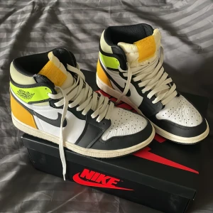 Nike Air Jordan 1 Retro High OG Volt - Snygga Nike Air Jordan 1 Retro High OG i en cool färgkombination av svart, vit, gul och neongrön. Skorna har klassisk snörning och kommer i originalkartong med extra snören. Perfekta för dig som vill sticka ut med stil.