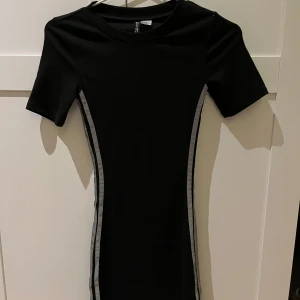 Klänning med reflex - Snygg svart klänning med grå reflexer längs sidorna. Klänningen har en tight passform och korta ärmar. Stretchig! Xxs
