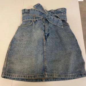 Jeanskjol med knytband - Passar både för xxs, xs och i vissa fall S. Trendig jeanskjol i blått med knytband i midjan och två stora bakfickor. Perfekt för en avslappnad stil med en touch av retro. Kjolen har en normal passform