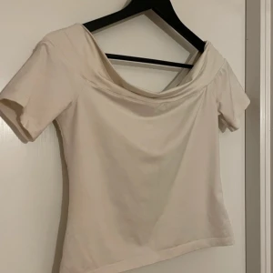 Beige offshoulder topp - Säljer en stilren beige offshoulder topp med korta ärmar. Perfekt för en avslappnad och chic look. Toppen har en mjuk och bekväm passform.