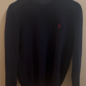 Mörkblå tröja från Ralph Lauren - Säljer en stilren mörkblå tröja från Ralph Lauren med det klassiska röda logotypbroderiet på bröstet. Tröjan har långa ärmar och är perfekt för en elegant och avslappnad look.