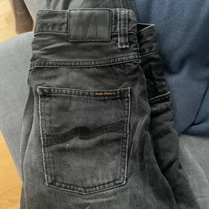 Svarta jeans från Nudie Jeans - Snygga svarta jeans från Nudie Jeans med klassisk femficksdesign. De har en diskret logga på bakfickan och en bekväm passform. Perfekta för en stilren look. Storlek 30/30
