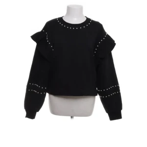 Svart tröja med volang och pärlor - Snygg svart tröja med volangdetaljer på axlarna och pärlor längs halsringningen och ärmarna. Perfekt för en stilren look med det lilla extra. Tröjan har långa ärmar och en normal passform. Storlek L men sitter som M