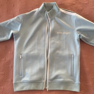 Ljusblå track jacket från Palm Angels /Bra pris!  - Säljer en snygg ljusblå track jacket från Palm Angels. Jackan har en dragkedja framtill, använd några gånger men ser ny ut, finns några jätte små fläckar men man lägger inte märke till dem.  Storlek S men passar M också. 