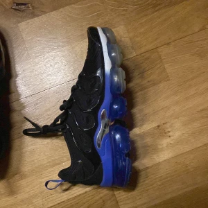 Nike sneakers med blå sula - Snygga Nike sneakers i svart med en iögonfallande blå sula. Skorna har snörning och en modern design med synliga luftkuddar i sulan för extra komfort. Perfekta för en sportig look.