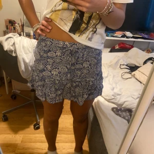 Blå blommig kjol från Zara - Säljer en blå kjol från Zara med blommigt mönster. Kjolen har en volangdetalj och även insydda shorts under! Den är i väldigt bra skick! Säljer den då jag har många andra liknande kjolar.💖