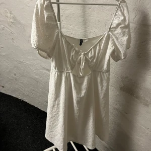 Vit klänning med puffärmar - Charmig vit klänning från H&M med puffiga kortärmar och knytning framtill. Klänningen har ett diskret blommigt mönster och en söt v-ringning. Perfekt för sommarens varma dagar. Man kan justera banden vid bysten