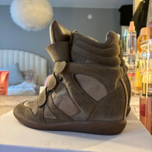 Isabel Marant  - Snygga brun/gröna Isabel Marant skor i mocka med kilklack och kardborreband. De har en unik design med vadderad ankel och perforerade detaljer på! Köpta här på plick men i ett väldigt fint skick🥰