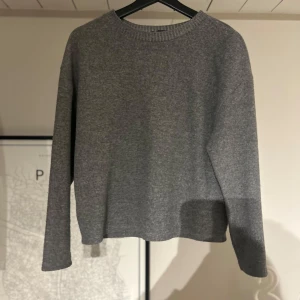 Grå stickad tröja - Säljer en stilren grå stickad tröja med rund halsringning. Tröjan har långa ärmar och en enkel design som passar perfekt för kyligare dagar. Perfekt för lager-på-lager eller som den är.