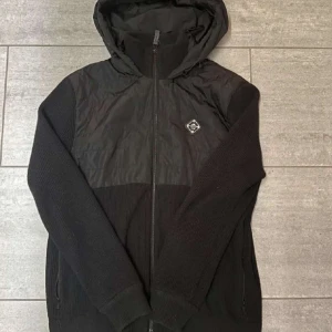 Svart jacka med huva från J.Lindeberg - Snygg svart jacka från J.Lindeberg med huva.  Stolek L men sitter som S/M. Köpt för 3000kr. Säljs inte längre. Pris kan diskuteras vid snabbafär 