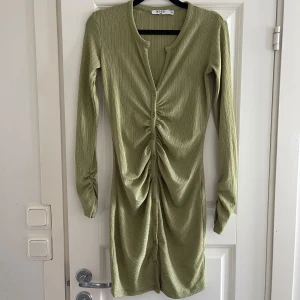 Olivgrön ribbad klänning med knappar - Snygg olivgrön klänning från NA-KD i ribbat material. Den har långa ärmar och en knäppning framtill som ger en cool rynkad effekt. Perfekt för en stilren look!