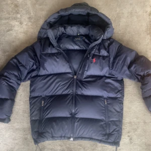 Mörkblå dunjacka från Ralph Lauren - Säljer en snygg mörkblå dunjacka från Ralph Lauren, bra skick bara att dragkjedan är lite strulig men FUNKAR och är en lätt fixning, hör av er vi fler frågor eller funderingar!