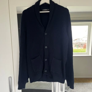 Mörkblå kofta från Dressmann - Säljer en stilren svart kofta från Dressmann i ribbstickat material. Den har använts flera gånger med är fortfarande i fint skick. Storlek M men sitter som en L. Säljer den för att den har blivit för kort för mig. Hör av dig vid funderingar😃