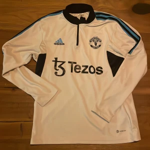 Vit långärmad Manchester United tröja från Adidas - Säljer en vit långärmad Manchester United tröja från Adidas med svarta och blå detaljer. Passar även S.