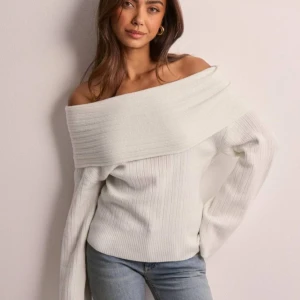 Vit offshoulder tröja - Säljer en stilren vit oanvänd offshoulder tröja från Nelly  med ribbad design. Tröjan har långa ärmar och en bred krage som ger en elegant look. Perfekt för en trendig och avslappnad stil💞nypris 399