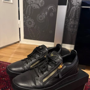 Giuseppe Zanotti skor - Snygga svarta sneakers i skinn från Giuseppe Zanotti med guldfärgade dragkedjor och snörning. Originella Dustbagen ingår. Skick är runt 8/10, de är sparsamt använda. Köpt från yoox där ord pris är 5200kr