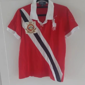 Ralph Lauren Polo - Polo Ralph lauren tröja storlek S. Snygg röd t-shirt från Ralph Lauren med korta ärmar och en vit krage. Den har ett stort broderat emblem på bröstet och en diagonal rand i vitt och svart. Perfekt för en stilren look! Pris kan diskuteras!