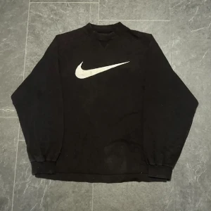 Svart tröja från Nike sweatshirt oversized  - Säljer en svart tröja från Nike med det ikoniska swoosh-logotypen i vitt på framsidan. Tröjan har långa ärmar och en rund halsringning. Perfekt för en sportig och avslappnad stil.