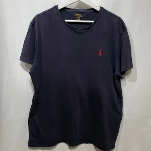 Mörkblå t-shirt från Ralph Lauren - Snygg mörkblå t-shirt från Ralph Lauren med det klassiska röda broderade logotypen på bröstet. Perfekt för en stilren och avslappnad look. Modellen är 180cm