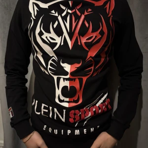 Phillip Plein tröja - Snygg svart långärmad tröja från Phillip pleins sport kollektion (plein Sport) med ett stort tigertryck i vitt och rött på framsidan. Trycket på ryggen har försvunnit lite i tvätten men annars i bra skick. Otroligt snygg och ovanlig tröja Ord pris ca 2500kr