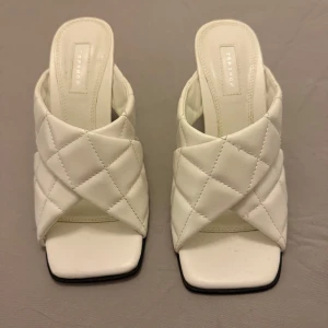 Vita quiltade klackskor från Topshop - Snygga vita klackskor från Topshop med quiltad design och öppen tå. Skorna har en fyrkantig tå och en elegant klack, perfekt för att lyfta din stil.