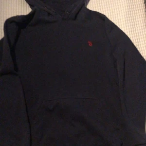 Mörkblå hoodie från Polo - Säljer en stilren mörkblå hoodie från U.S. Polo Assn. med en liten röd logga på bröstet. Perfekt för en avslappnad look.
