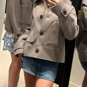 Beige kappa med knappar från Kappahl - Snygg beige kappa med stora knappar och långa ärmar. Jackan har en klassisk design med två stora fickor framtill och en rak passform. Perfekt för höst och vår. Nypris var 900kr och den har varit använd 2 ggr.