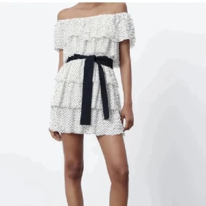 Vit offshoulder klänning med prickar -  vit offshoulder klänning med små svarta prickar och volangdetaljer. Klänningen har en svart knytband i midjan. Aldrig använd. 