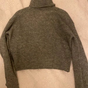 Grå ribbad polotröja - Säljer en stilren grå ribbad polotröja med croppad passform. Perfekt för kyligare dagar med sin höga krage och långa ärmar. En mysig och trendig tröja för garderoben!