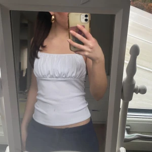 Vit ribbad topp från New Look - Säljer en vit ribbad linnetopp från New Look. Toppen har en smickrande rynkad detalj framtill och breda axelband. Perfekt under sommaren!