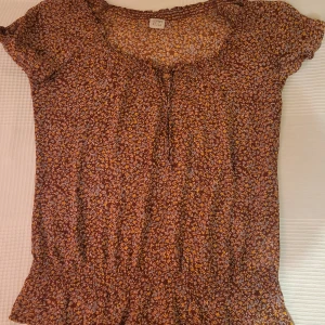 Blommig topp från Esprit - Säljer en söt blommig topp från Esprit i rött med små blommor i blått, gult och rosa. Toppen har korta ärmar och en rund halsringning. Perfekt för en avslappnad stil.