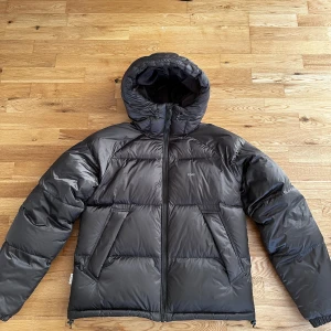 Brun  dunjacka från Yoke - Säljer en brun dunjacka från Yoke med huva och dragkedja. Jackan har en pufferdesign och är perfekt för kalla dagar. Den har två stora fickor framtill och justerbar dragsko vid huvan. Nypris 1999kr 