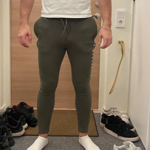 Gröna mjukisbyxor från Gymshark - Säljer ett par gröna mjukisbyxor från Gymshark. Byxorna har en tight passform med snörning i midjan och är perfekta för träning. De har en diskret logga längs benet och är tillverkade i ett mjukt och bekvämt material.