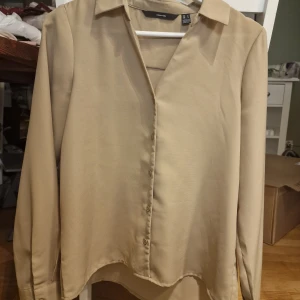 Beige blus från Vero Moda - Snygg beige blus från Vero Moda i storlek S. Blusen har långa ärmar och knappar framtill. Perfekt för en stilren look.