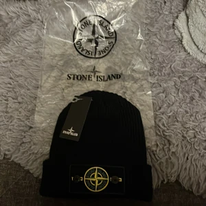 Svart ribbad mössa från Stone Island - Snygg svart ribbad mössa från Stone Island med det ikoniska broderade märket framtill. Perfekt för att hålla värmen med stil.