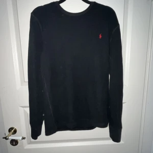 Ralph lauren tröja - Snygg svart långärmad tröja från Ralph Lauren med det klassiska röda logotypen på bröstet. Perfekt för en stilren och avslappnad look. Passar bra till både jeans och chinos.