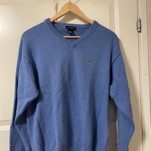 Blå tröja från GANT - Säljer en stilren blå tröja från GANT med v-ringning och ribbade kanter. . Tröjan har en liten broderad logga på bröstet.